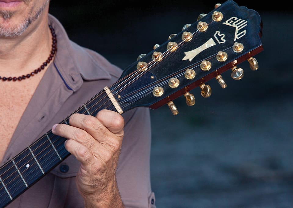 A close-up of JJ Grey holding his guitar. His chin, part of his chest and his hand are visible as he holds the strings of his instrument.