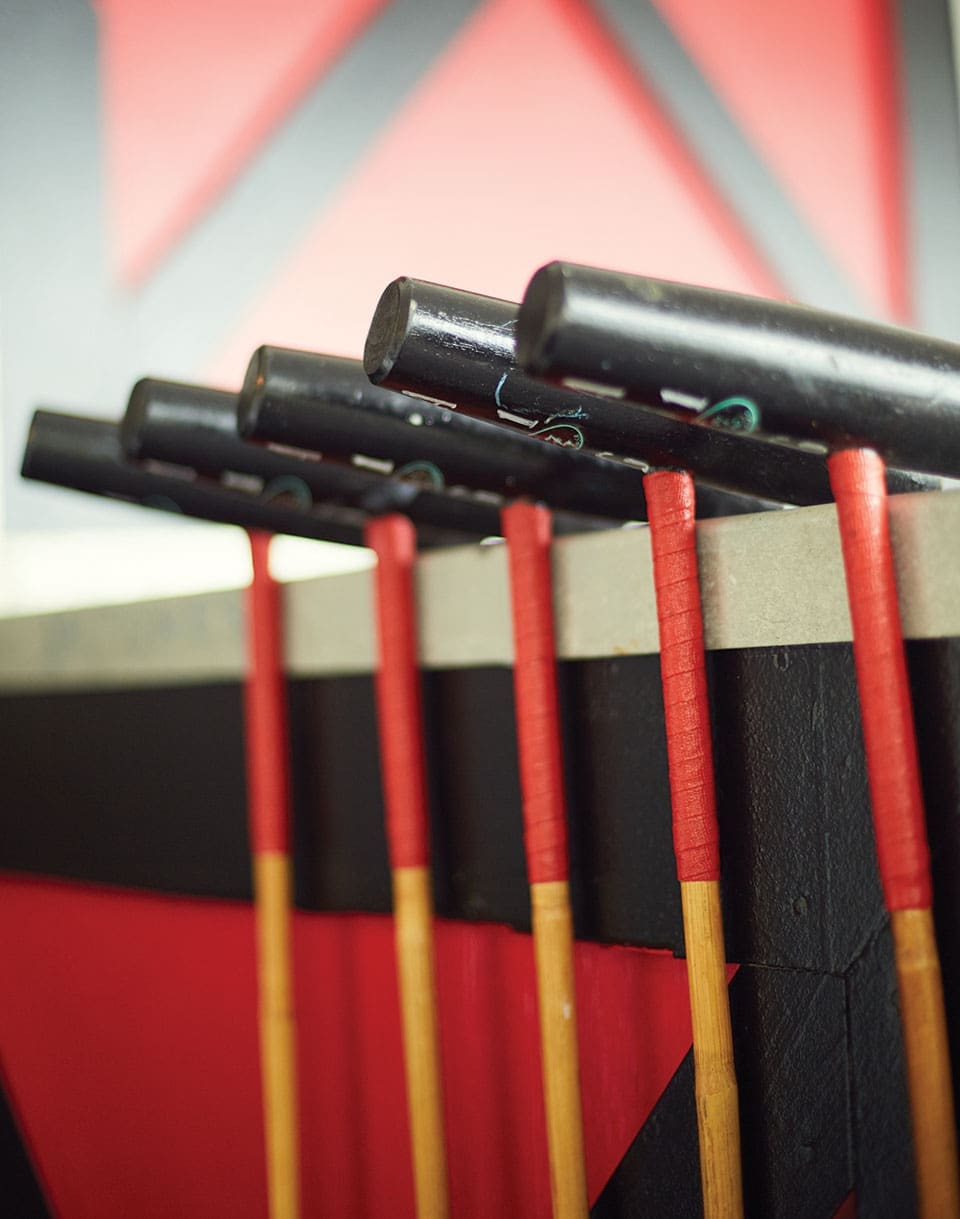 Five polo mallets with black tops and wooden and red handles.