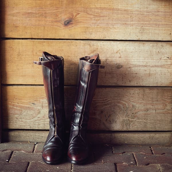 Brown riding boots stand up against a wooden wall. 