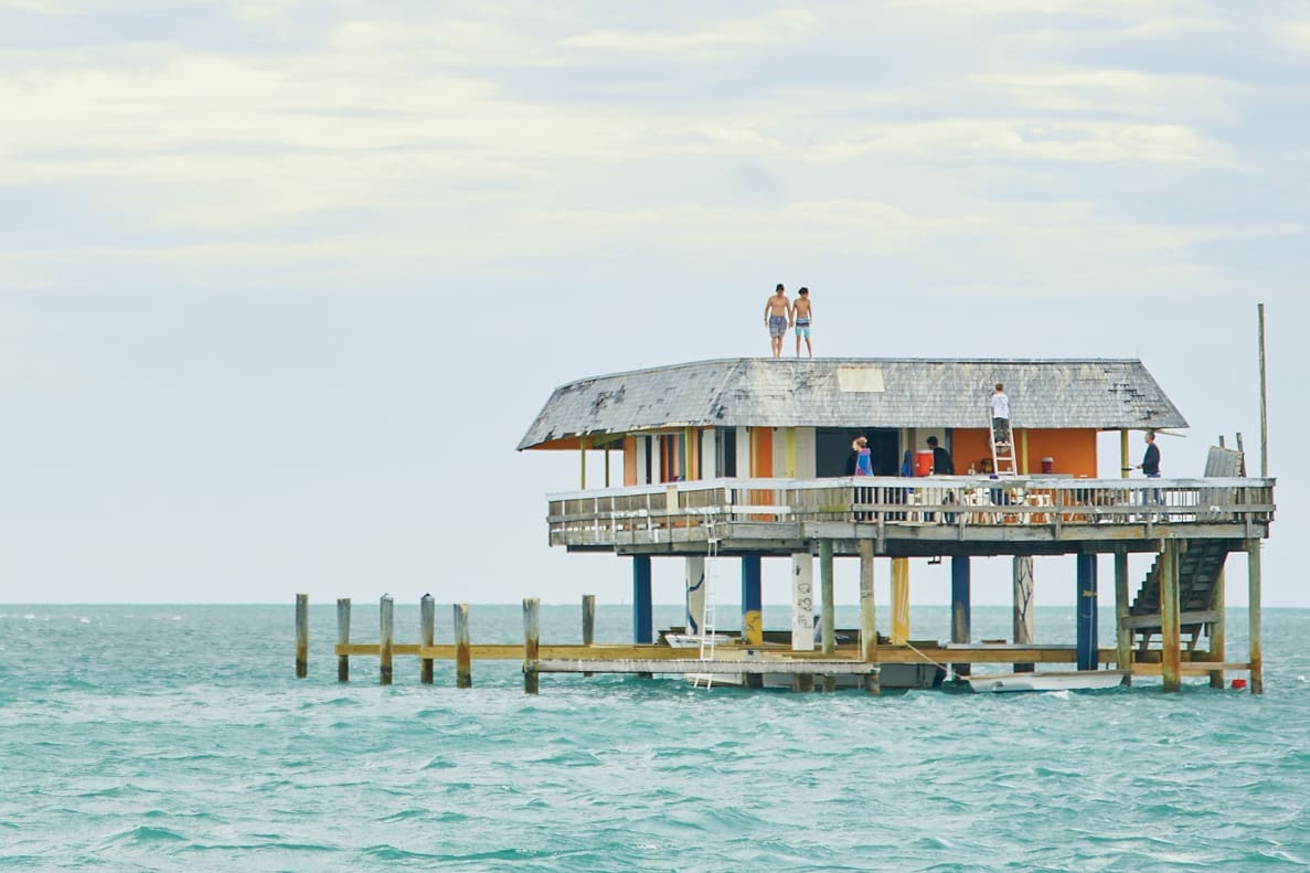 Stiltsville: Stilted, Jilted & Re-builted 1 Two boys standoff the roof of a Stiltsville home. Other people are visible on the homes deck.
