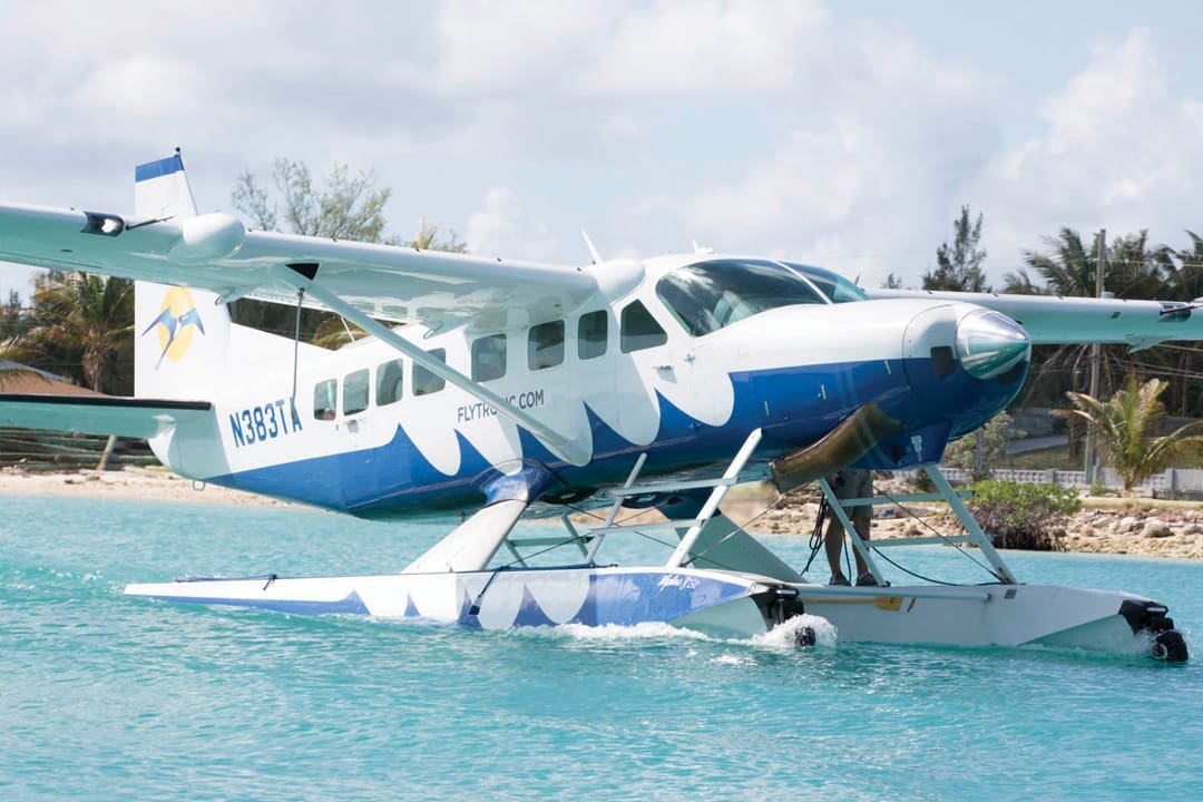 A blue and white seaplane that brings tourists to the Bahamas floats on the water. Numbers and letters on the plane read N383TA. It also says flytouwrist.com.