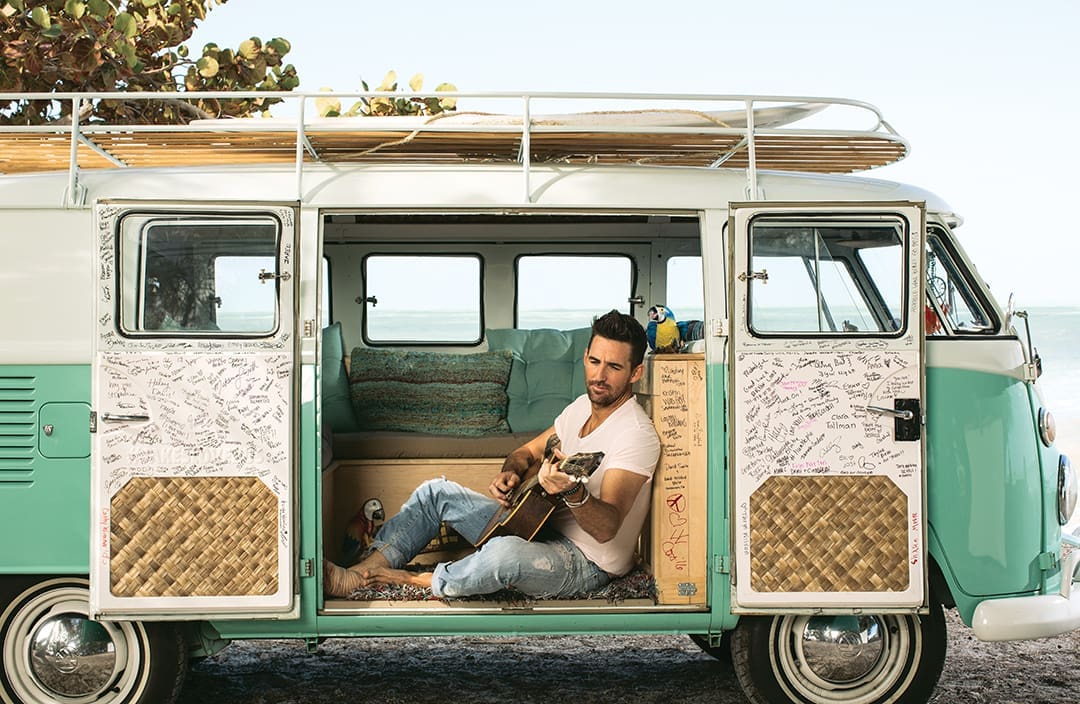 Jake Owen: The Sunshine Son 3 In 2017, Owen drove what he called the “love bus.” In this photo, Owen sits in a vintage van parked at a beach and plays guitar.