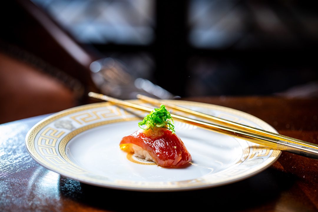 Zuke Akami rests on a white and gold plate with gold chopsticks.