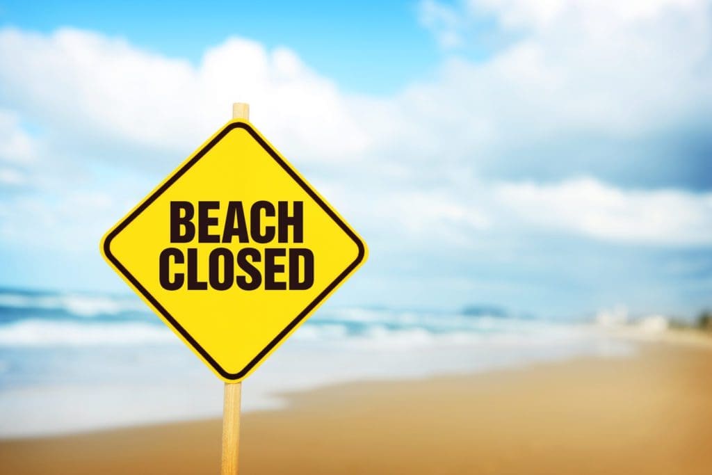Beach Closed on a yellow warning sign with wooden post at the beach