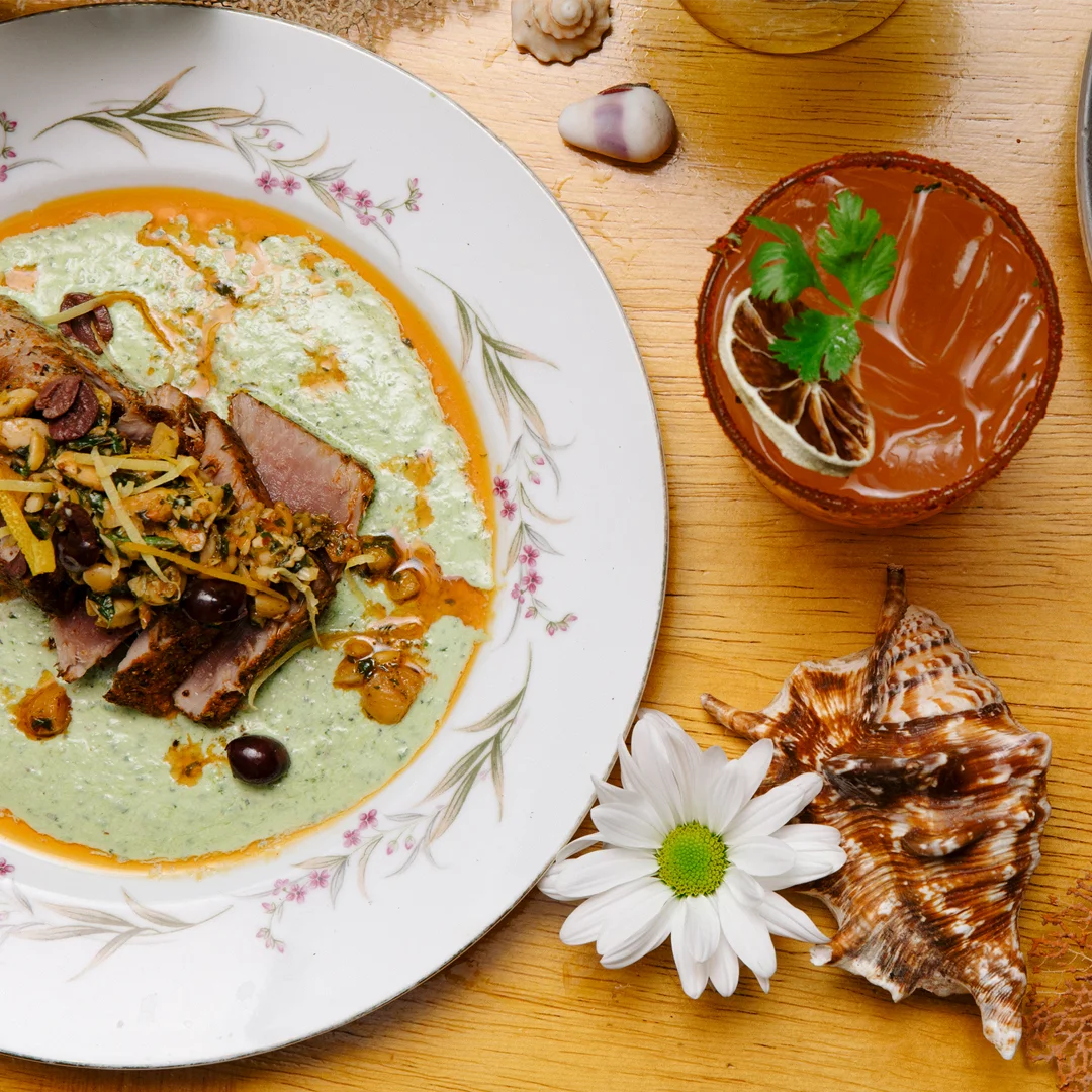 A tuna dish garnished with goat cheese and herb sauce, served with a cocktail.