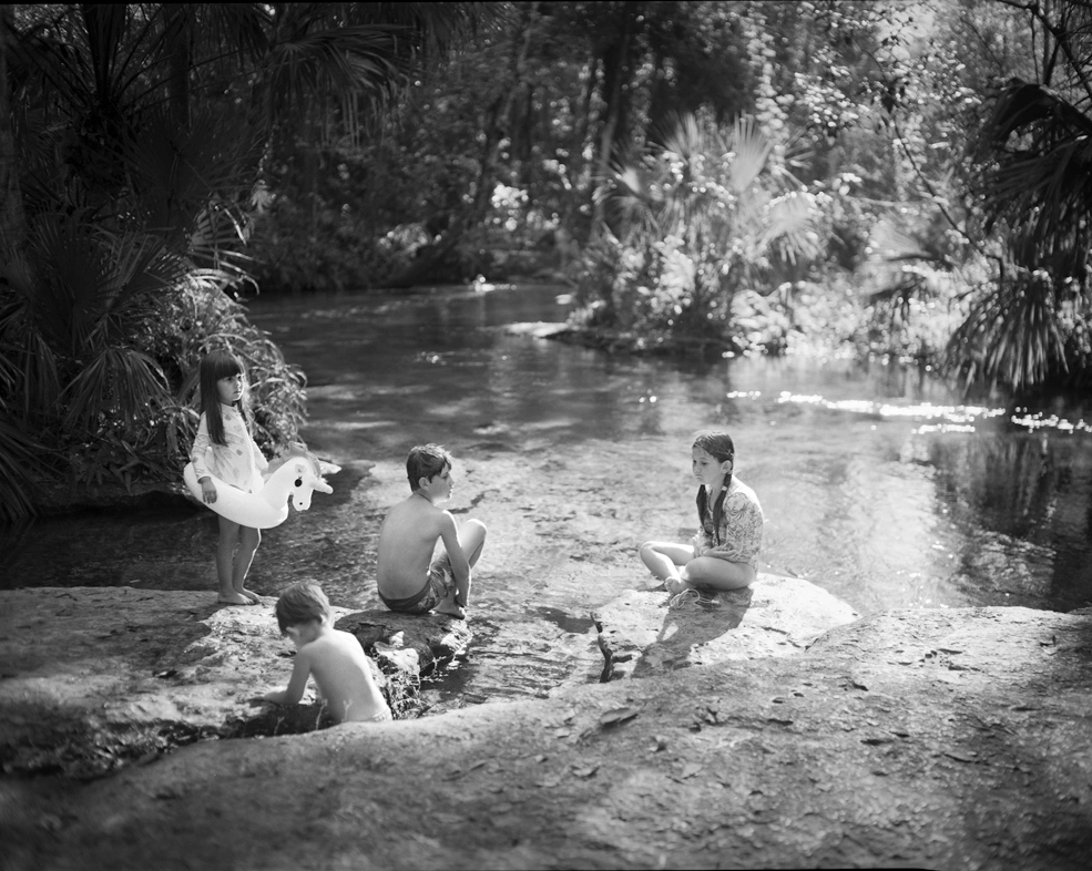 A Wild Florida Childhood Captured on Camera 9 kids sit on a rock by a spring in Central Florida
